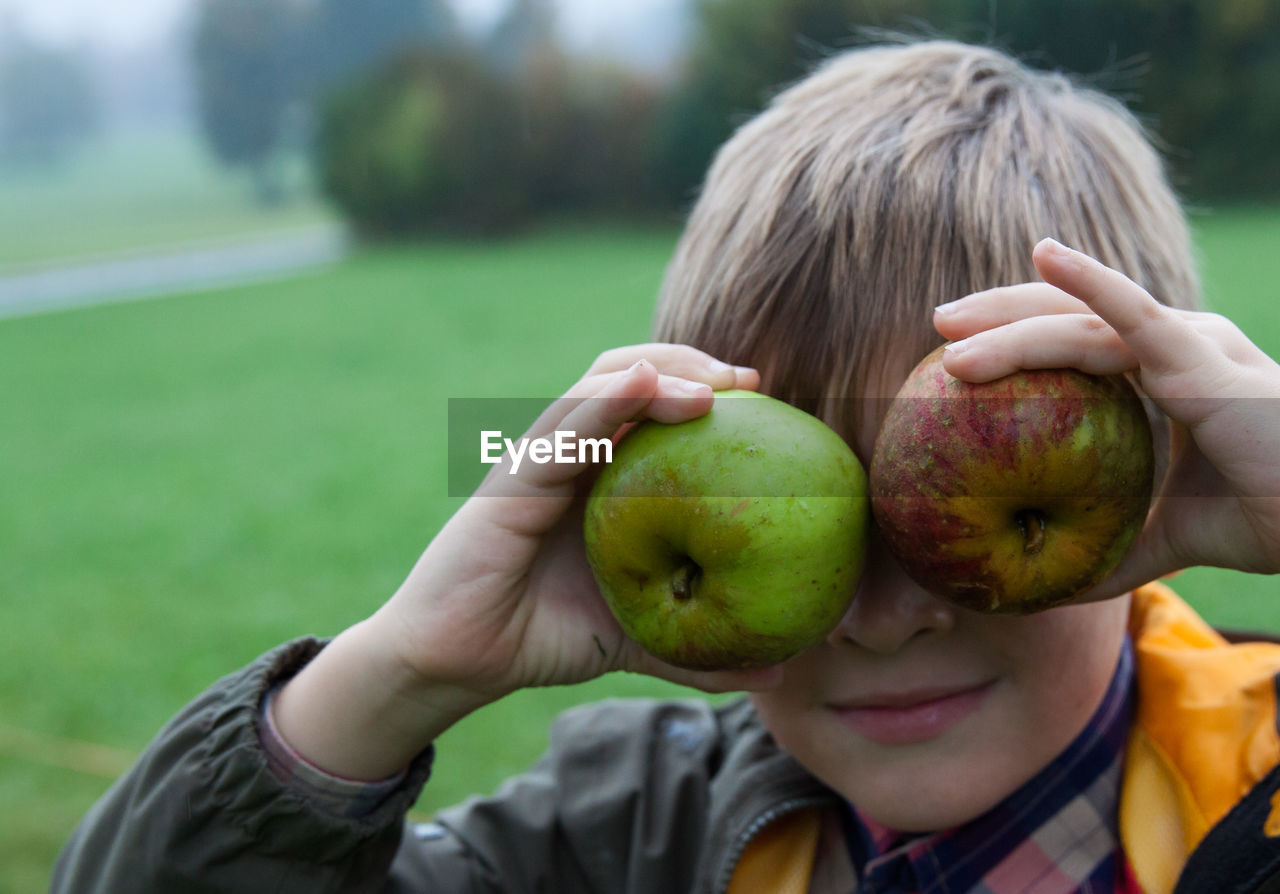 Close-up boy holding apples on his eyes