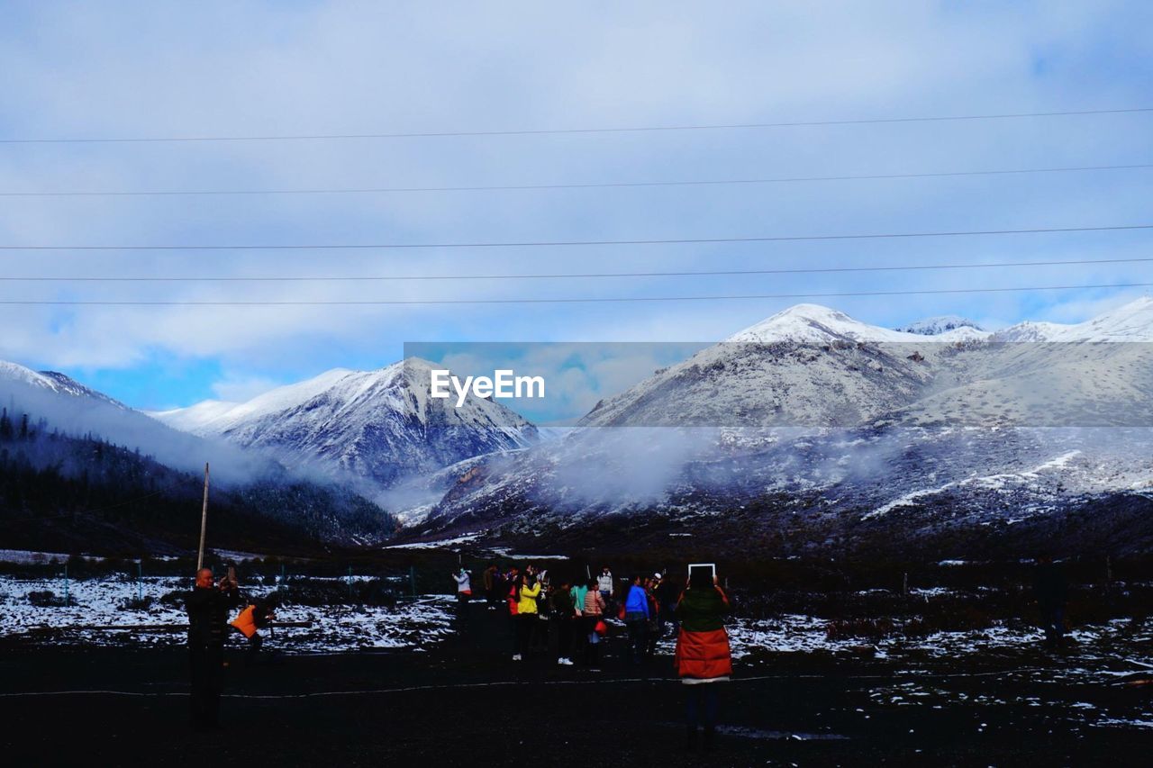 Tourists on field against snowcapped mountains