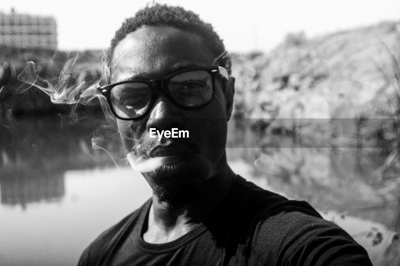 Portrait of mature man wearing eyeglasses while smoking against lake