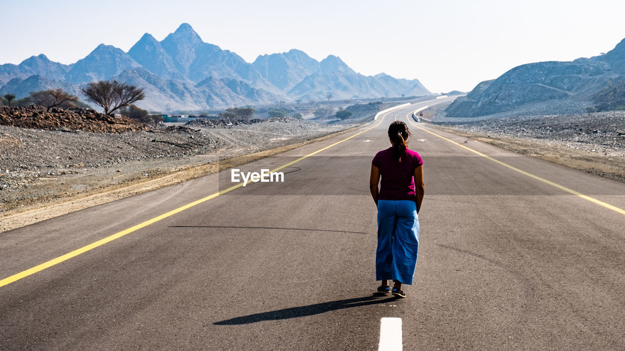 Rear view of woman standing on road against mountain range