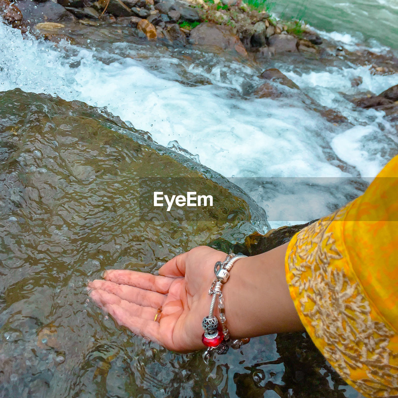 Cropped hand touching flower water in river