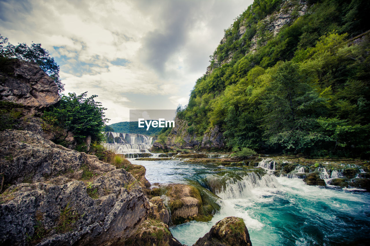 Scenic view of waterfall in forest against sky