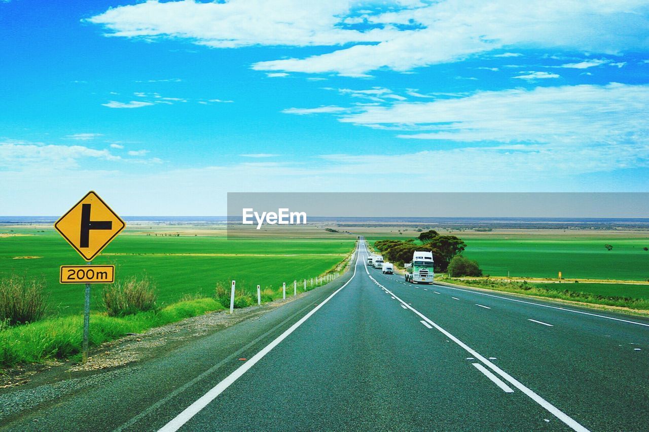 Road by agricultural landscape against sky