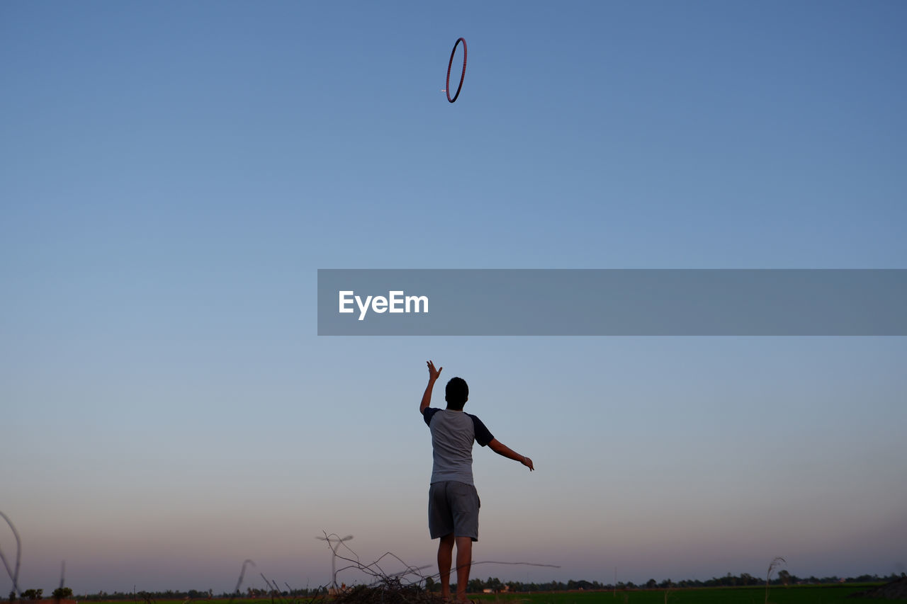 Rear view of man playing plastic hoop against clear sky at sunset