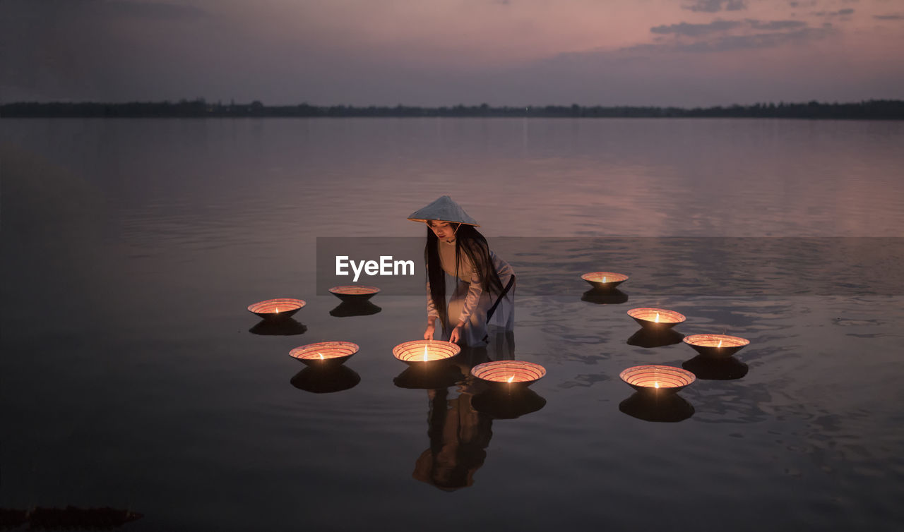 Woman by illuminated diyas in lake