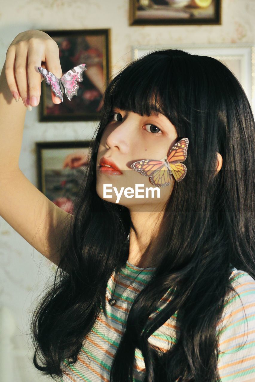 Portrait of young woman with artificial butterflies on face