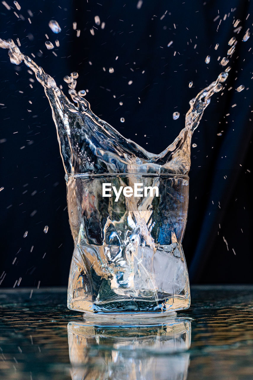 Close-up of water splashing on glass against black background