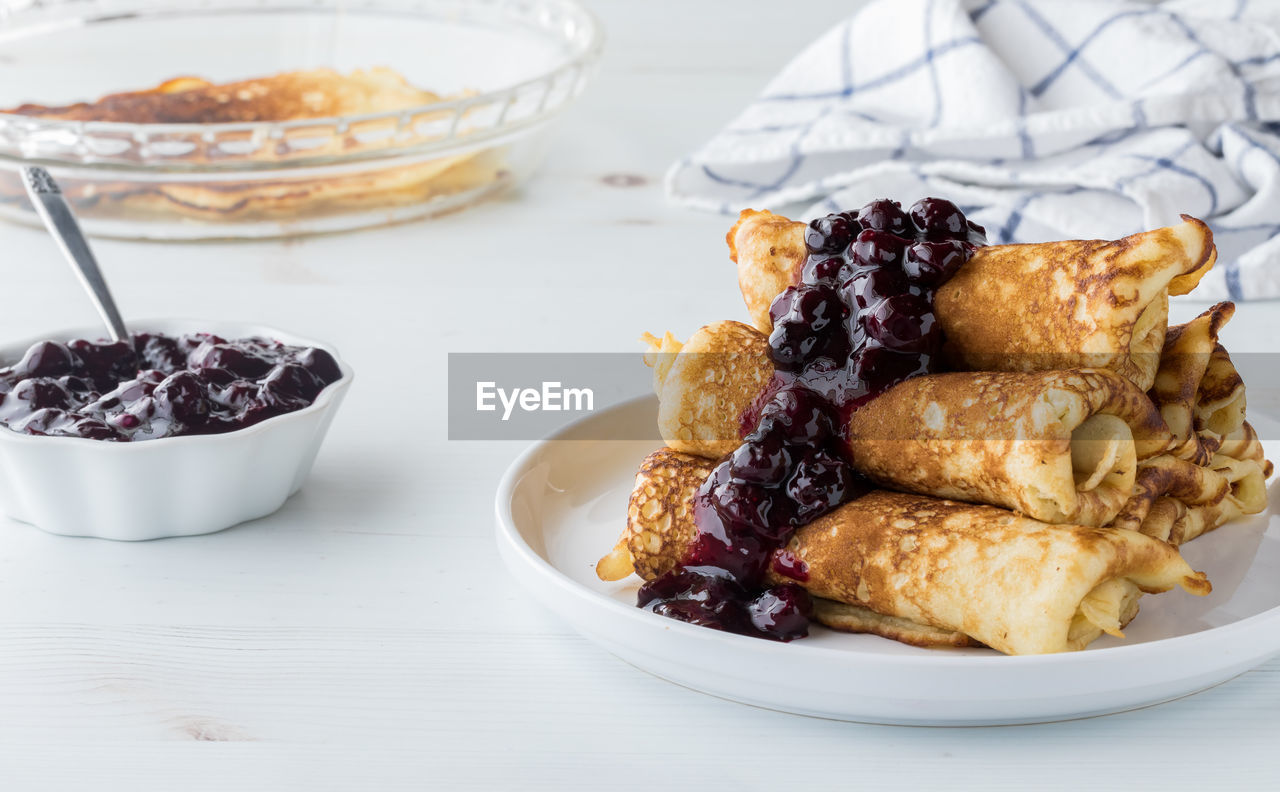 A pile of freshly made crepes topped with sweet blueberry sauce.