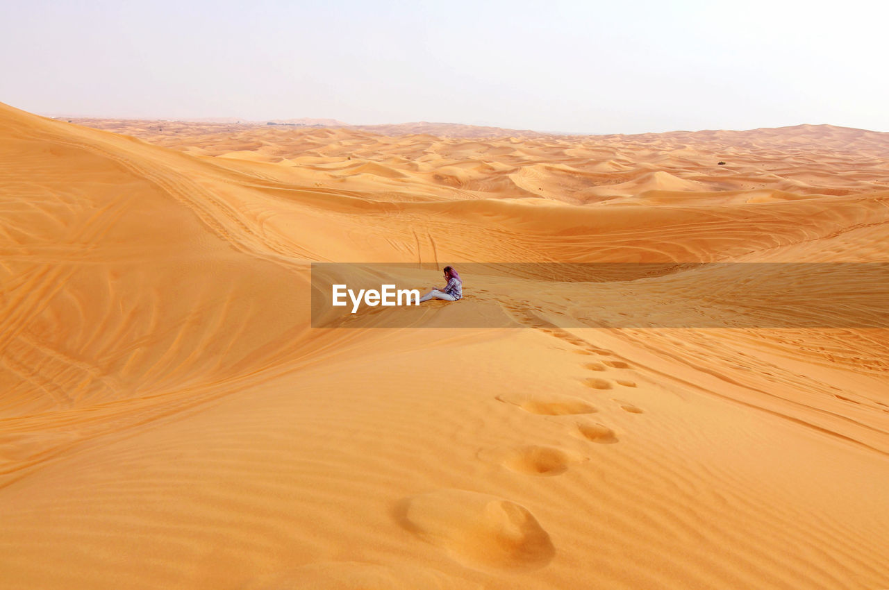 Young woman sitting on sand dune against clear sky