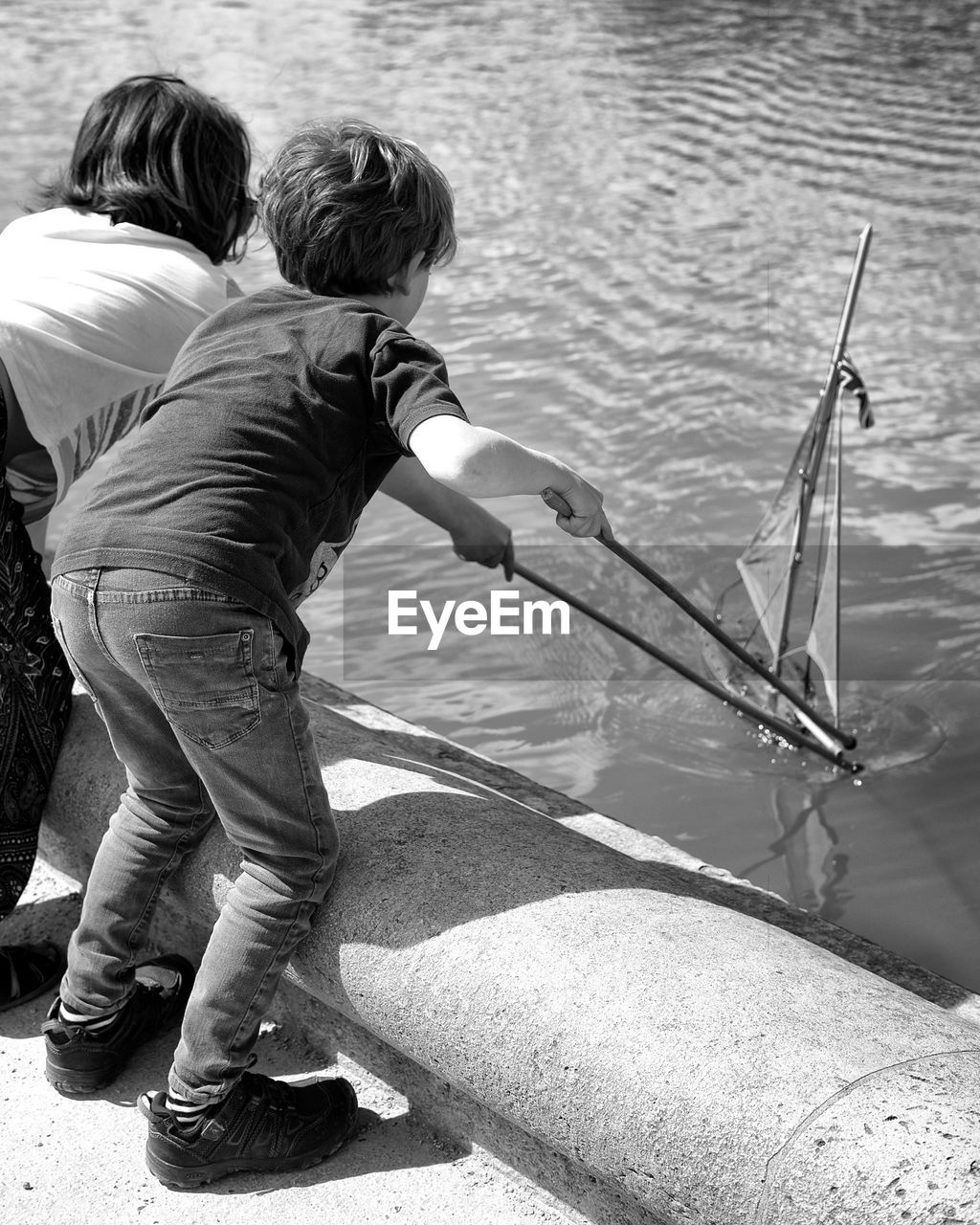 Rear view of siblings playing with toy boat in lake