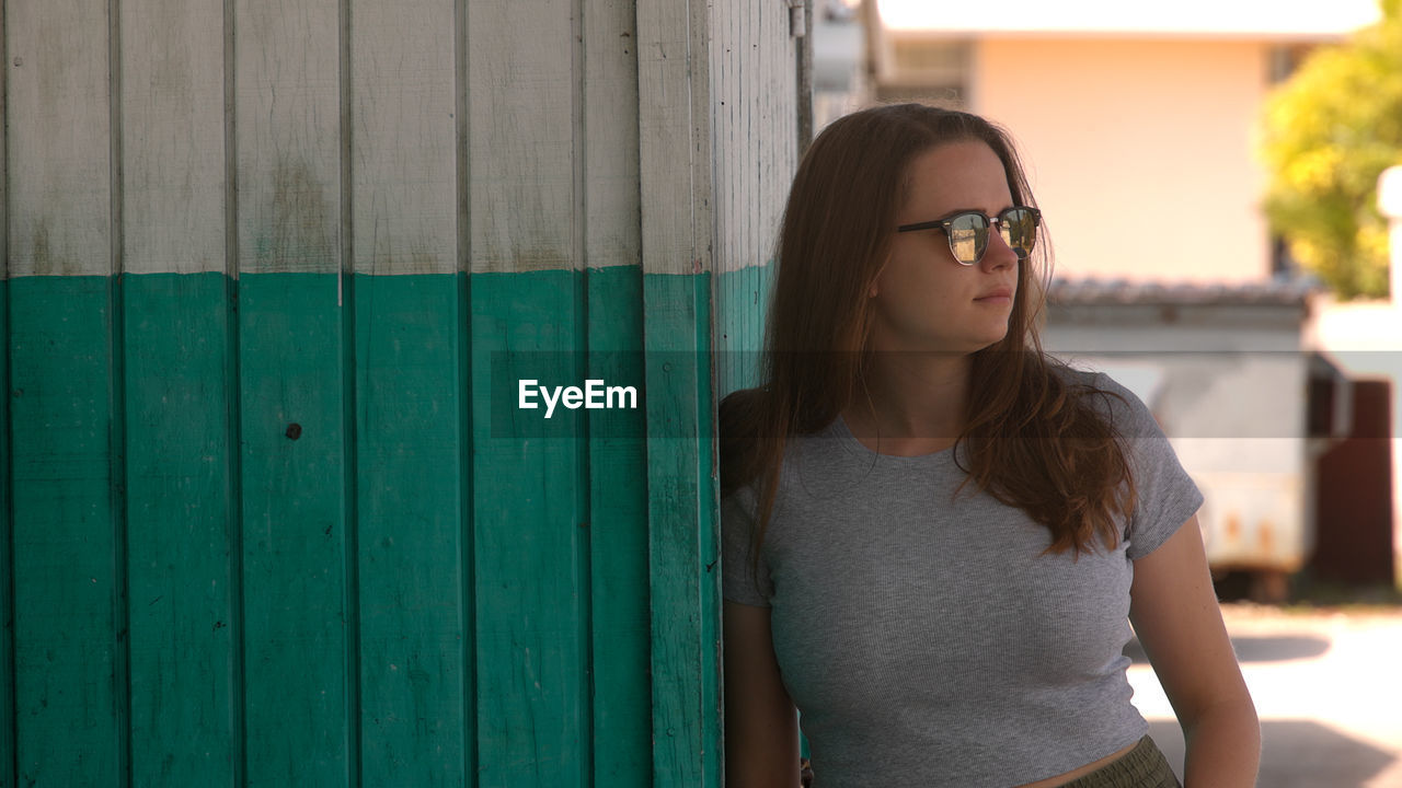 portrait of young woman wearing sunglasses standing against yellow wall