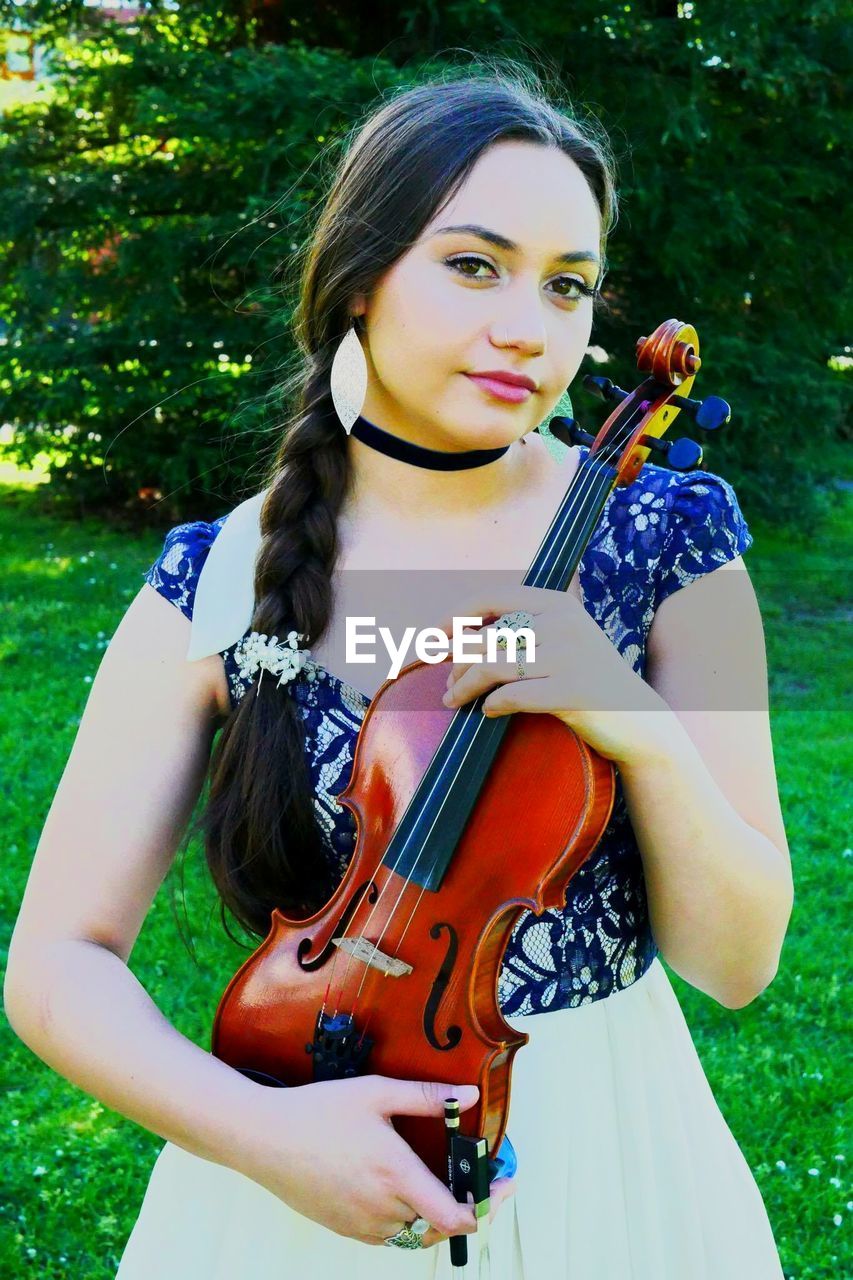 Portrait of beautiful young woman holding violin at park