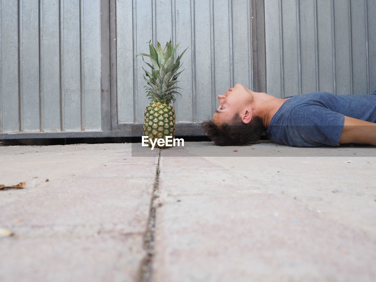 Surface level of young man looking at pineapple while lying on footpath