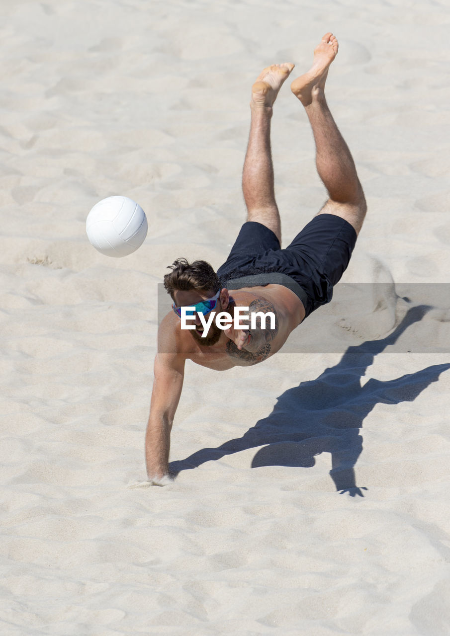 Shirtless man playing volleyball at beach