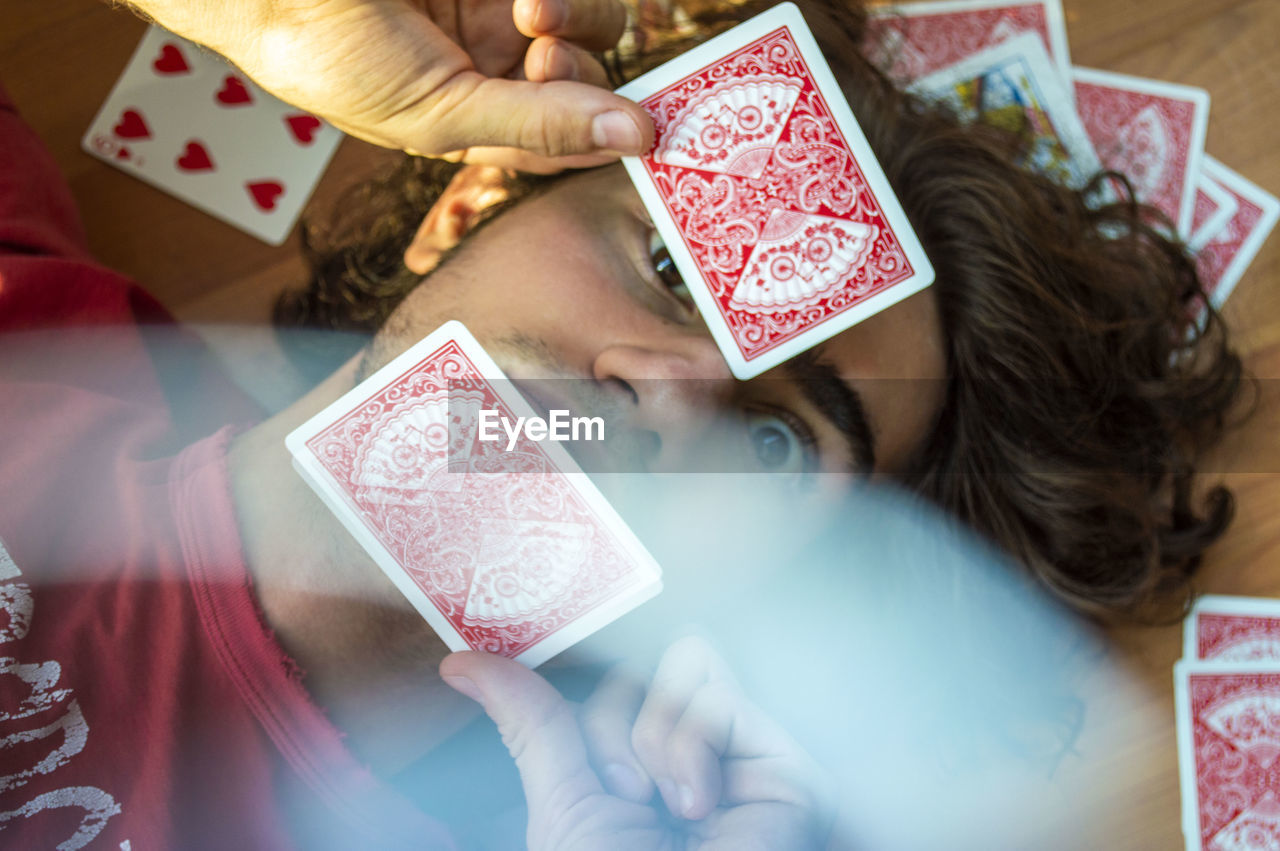 High angle view of man with playing cards lying on hardwood floor