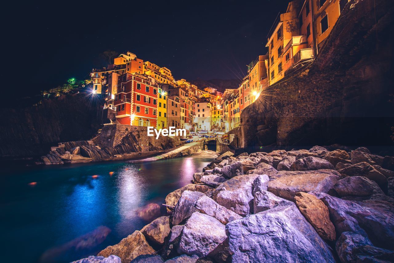 Illuminated building by river against sky at night