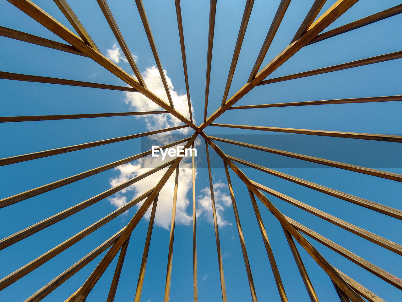 Wooden structure seen from below, with blue sky and small clouds on top.