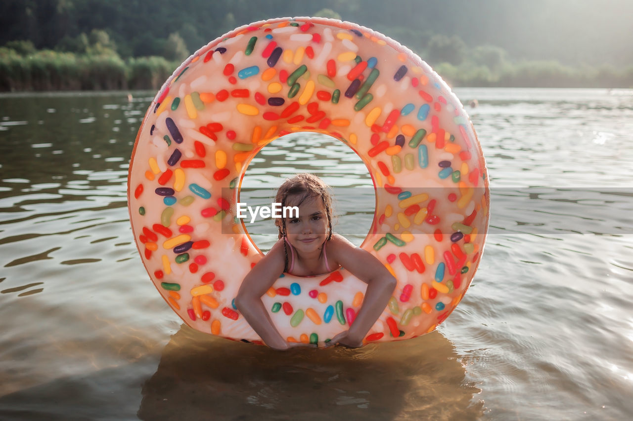 Girl swims with big donut inflatable ring on lake on hot summer day, happy summertime, cottagecore