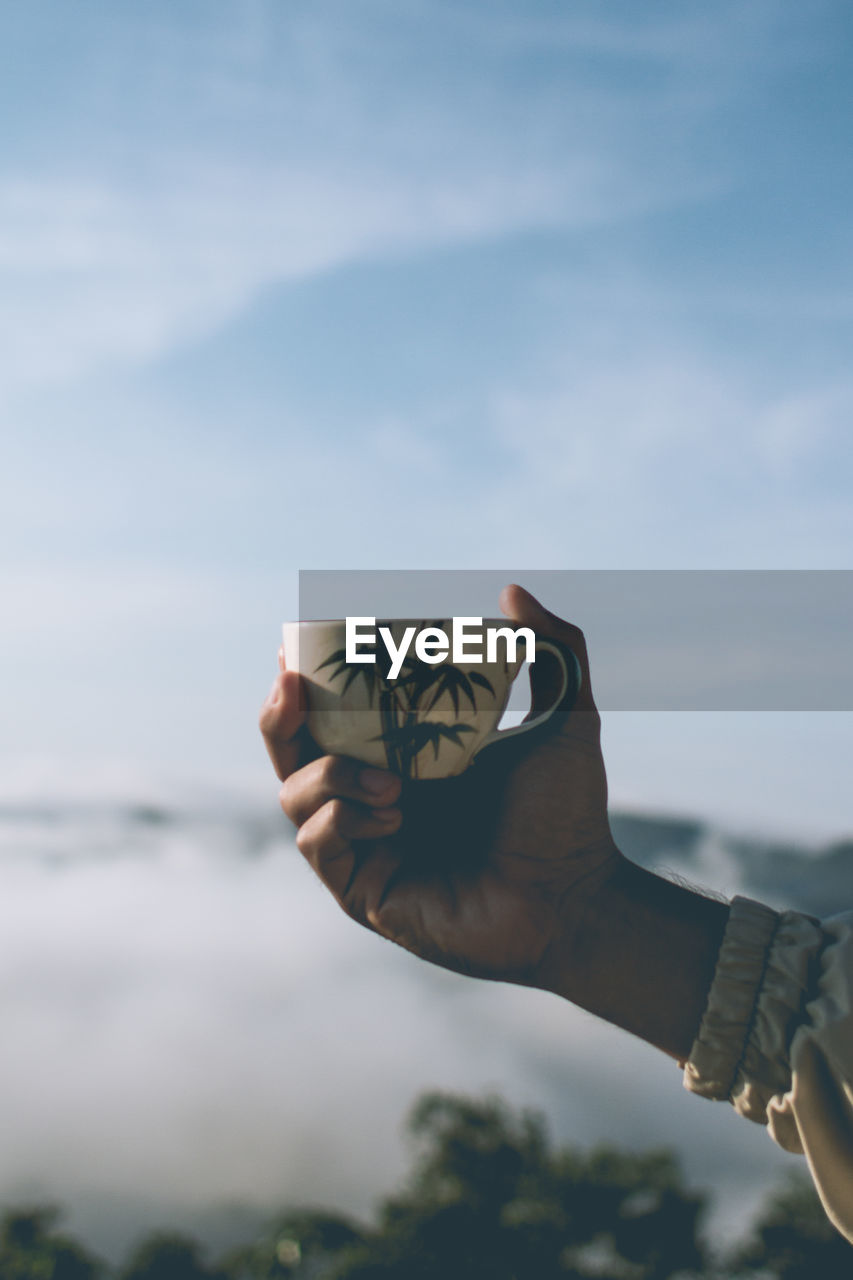 Midsection of person holding coffee cup against sky