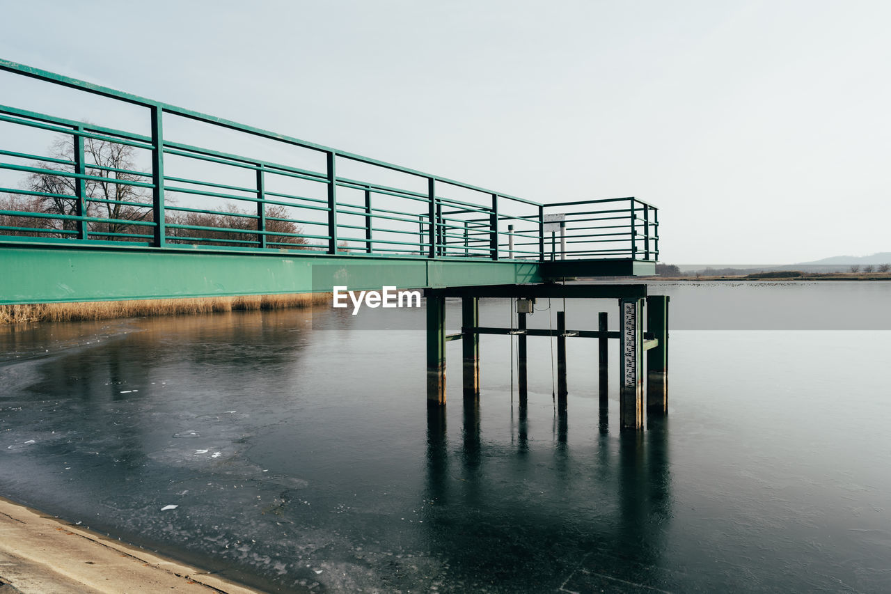 Railing by lake against clear sky