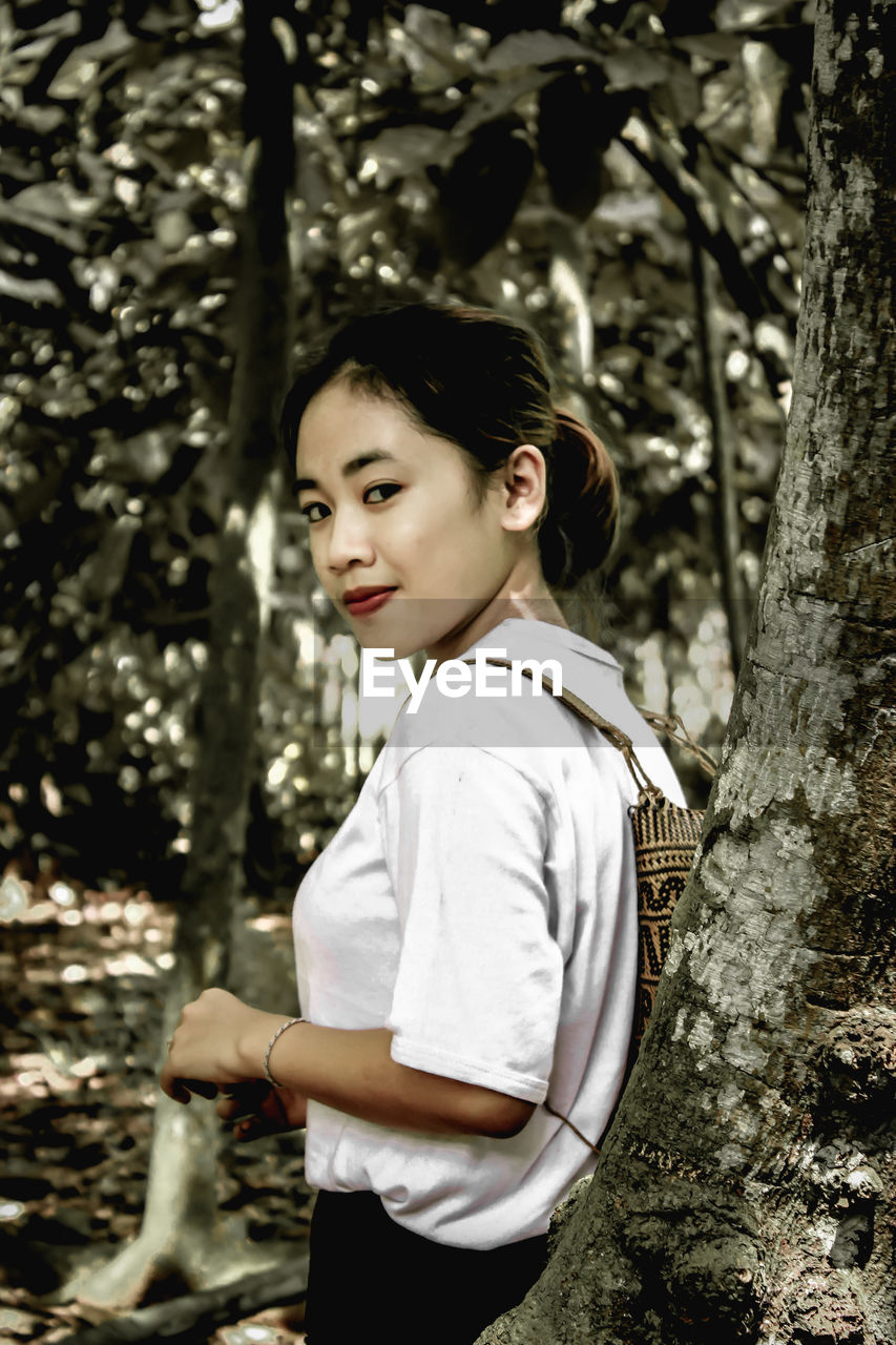 Portrait of woman standing on tree trunk