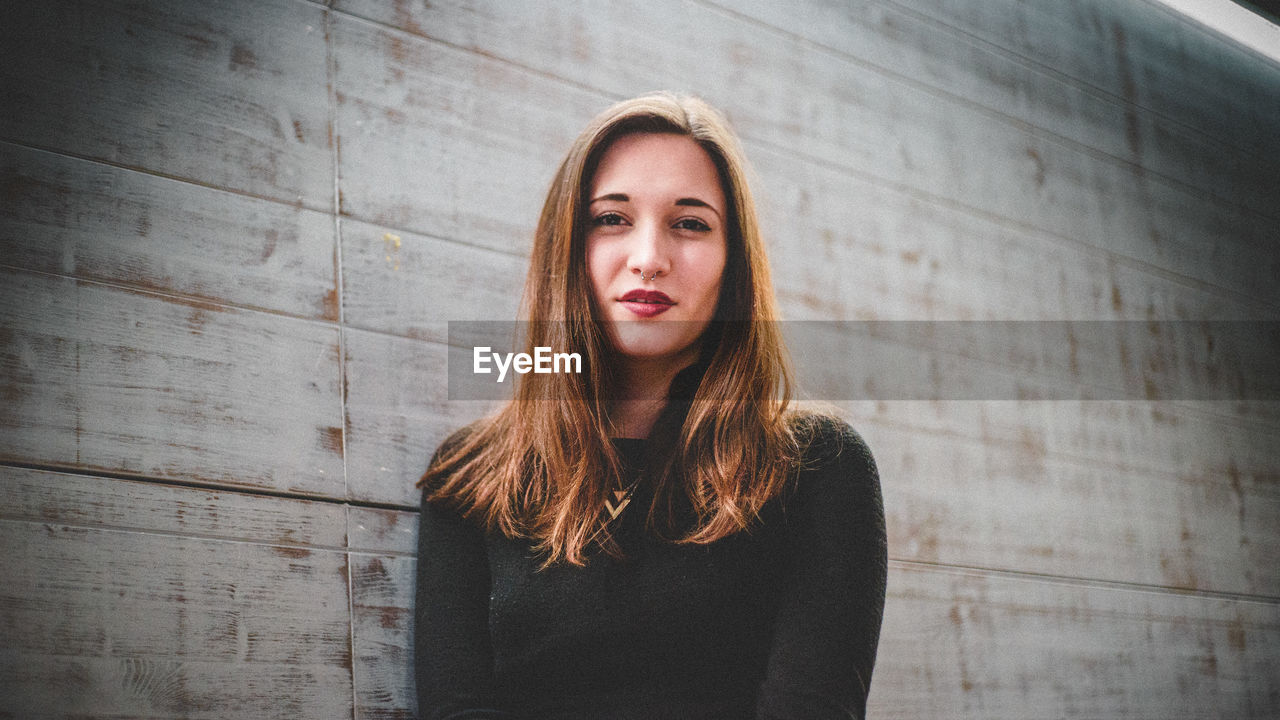 Portrait of young woman standing against wooden wall