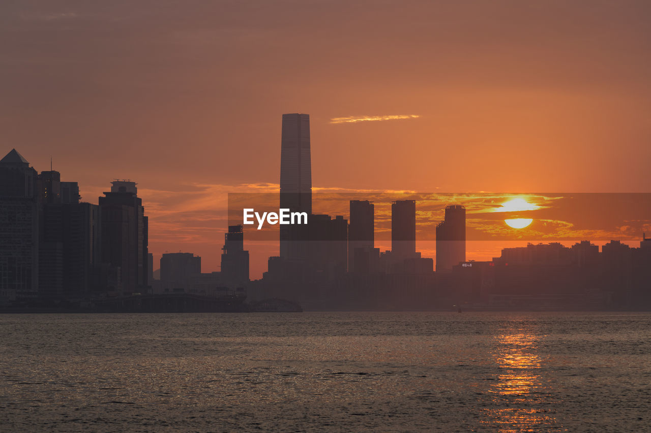 Silhouette buildings by sea against sky during sunset