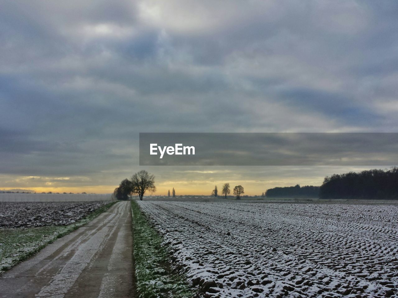 Pathway amidst snow covered field against cloudy sky