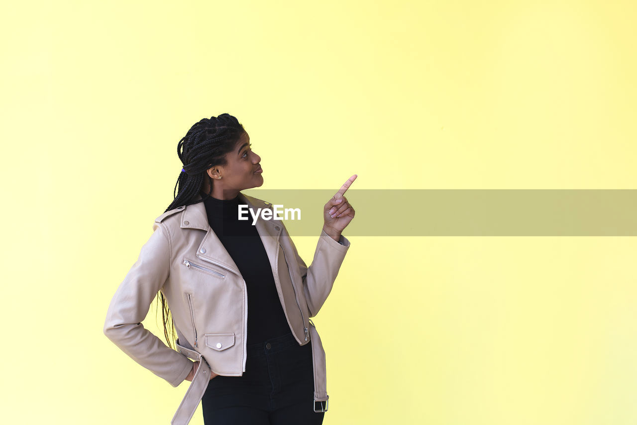 YOUNG WOMAN STANDING AGAINST GRAY BACKGROUND