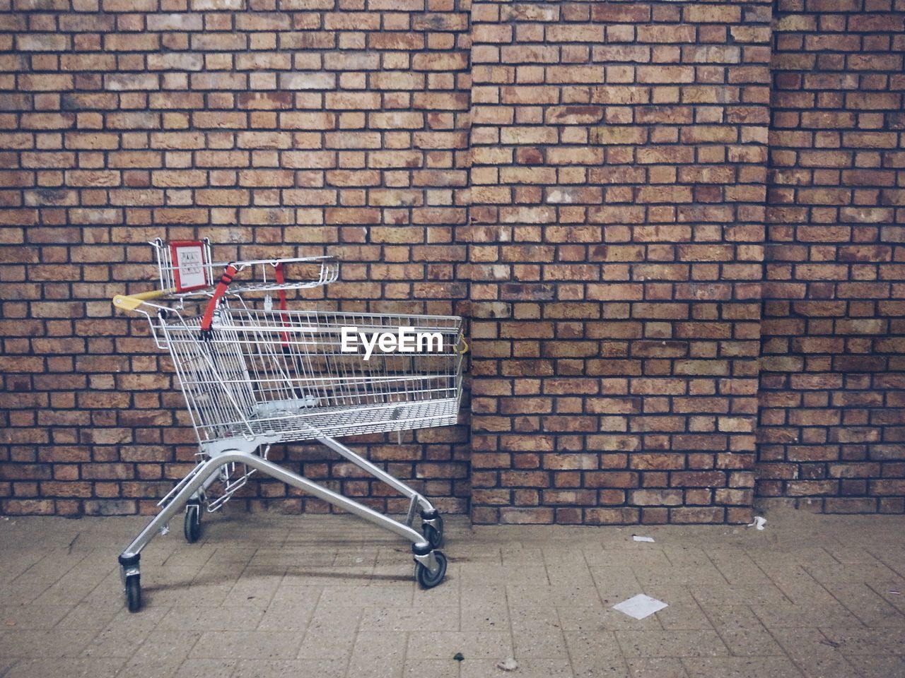 Shopping cart on sidewalk against brick wall