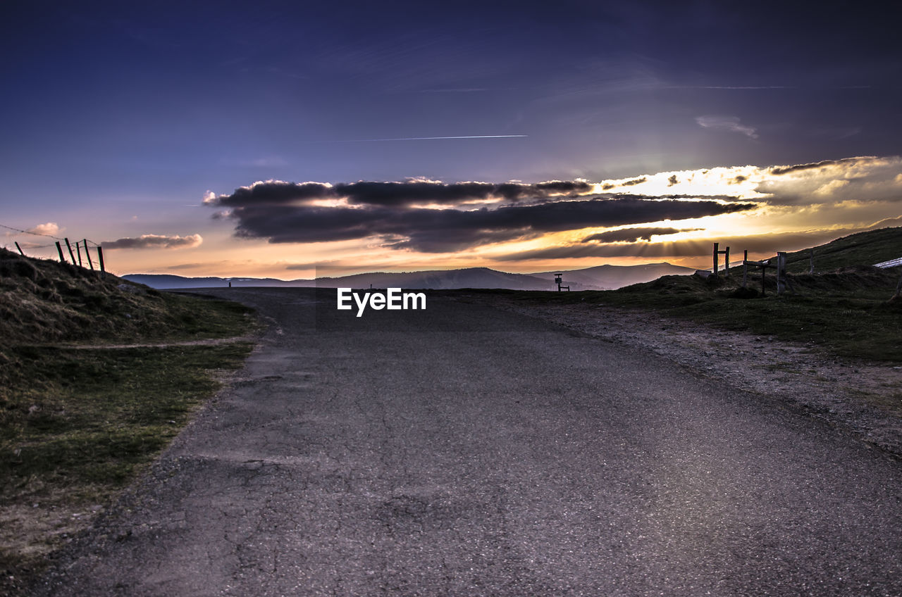 Road by landscape against sky during sunset