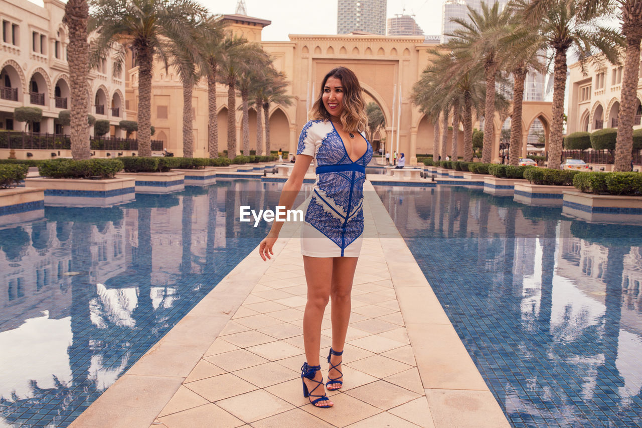 Woman standing by swimming pool against building