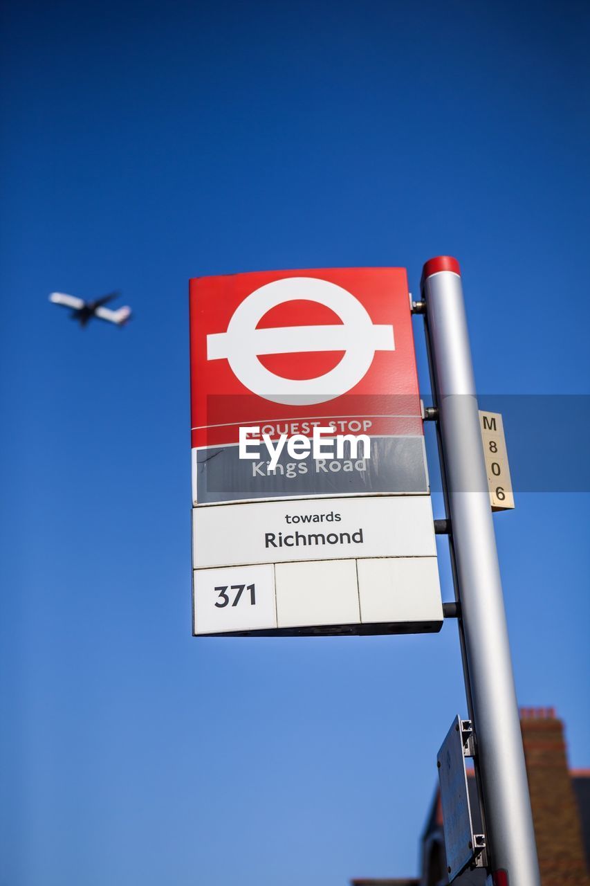 Low angle view of bus stop sign against clear blue sky