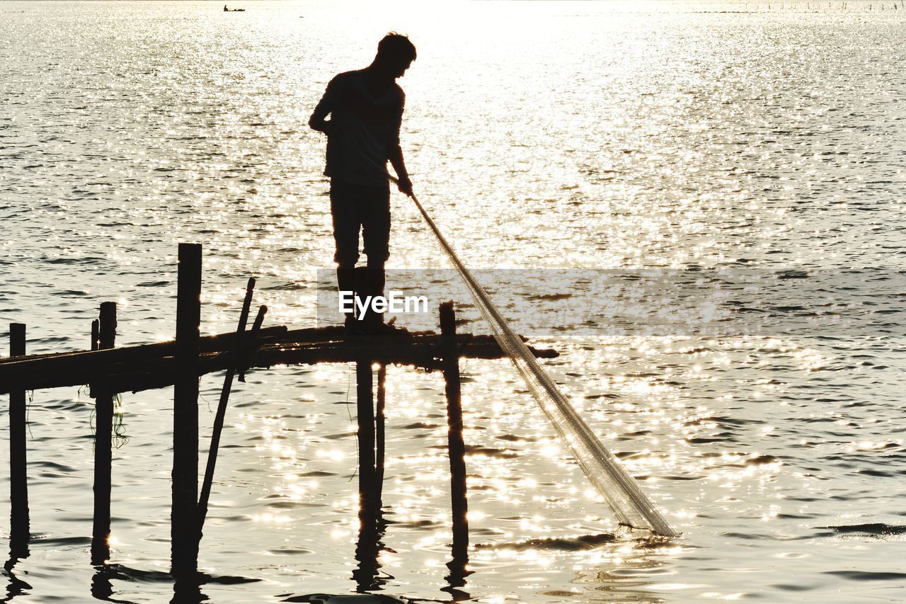 SILHOUETTE MAN STANDING AT SEA SHORE AGAINST SKY