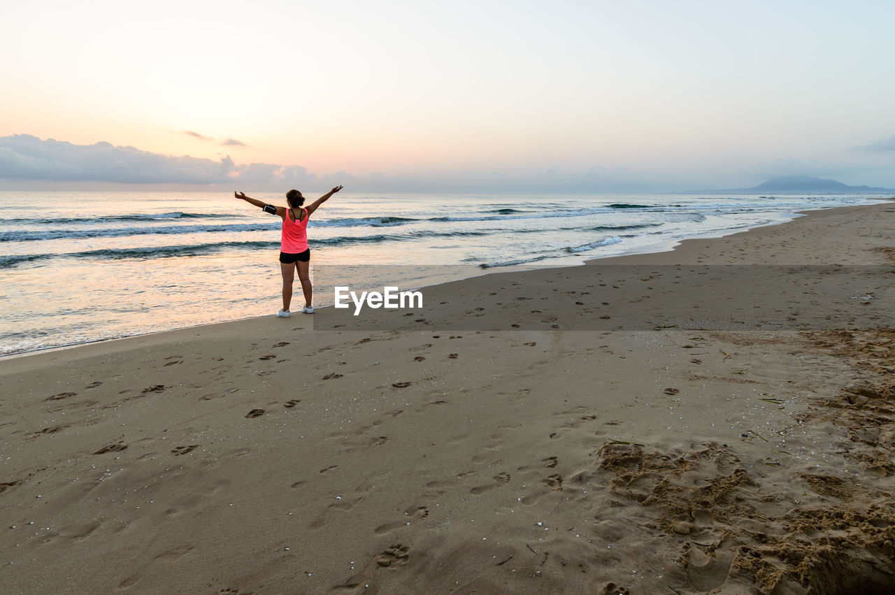 Rear view of woman with arms outstretched at beach against sky