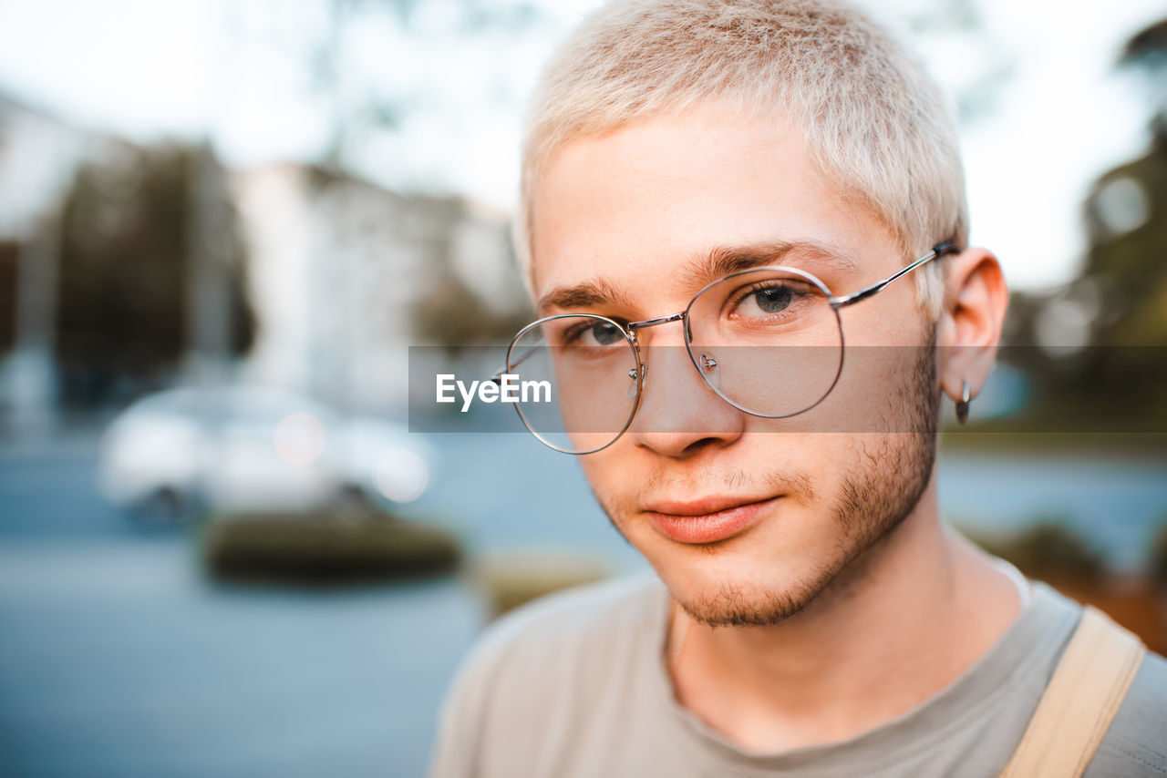 Handsome young man with blond short cut hairstyle wear glasses over urban city background outdoor. 