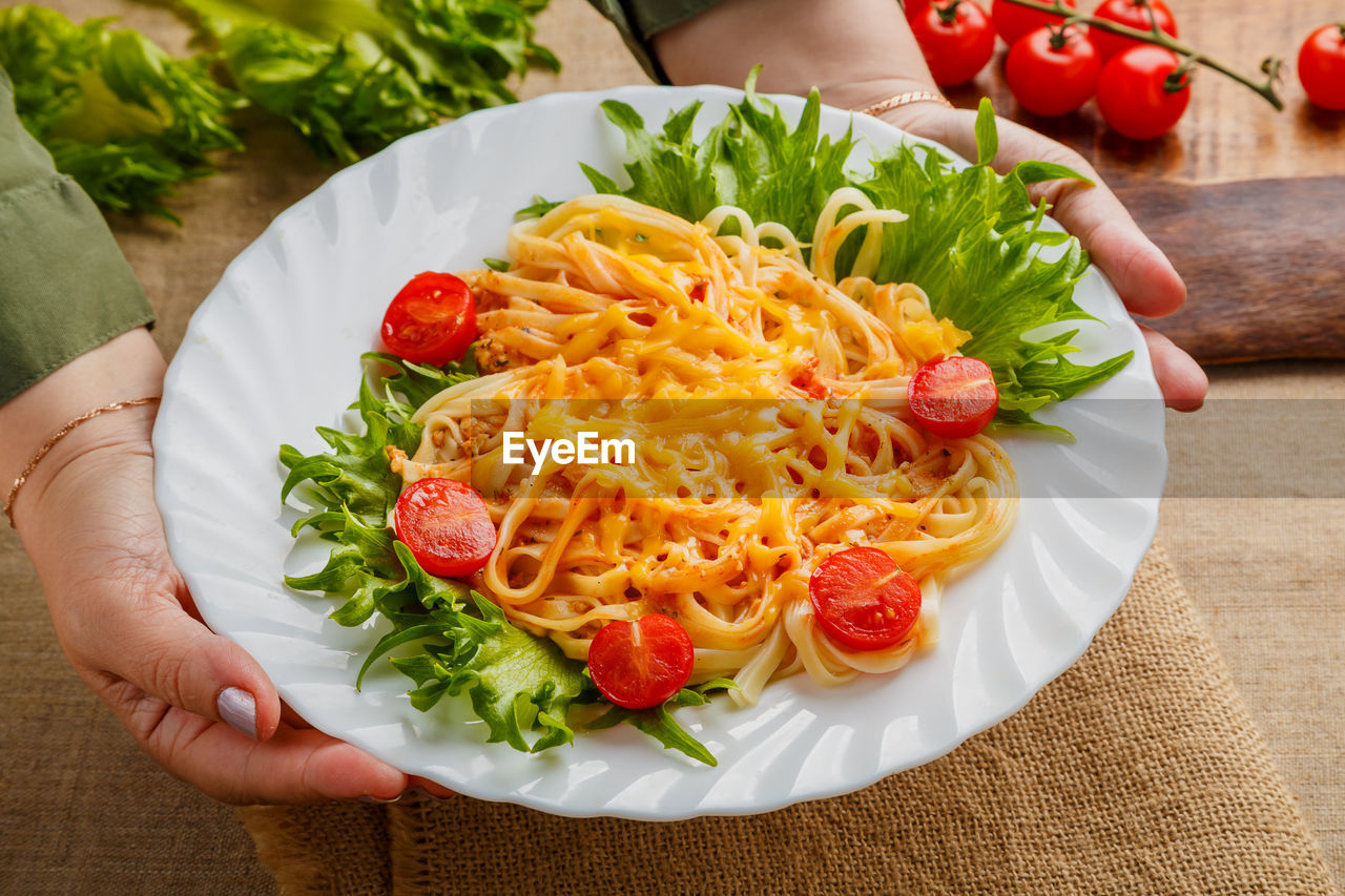 A plate of pasta with cherry tomatoes and cheese in female hands. horizontal photo