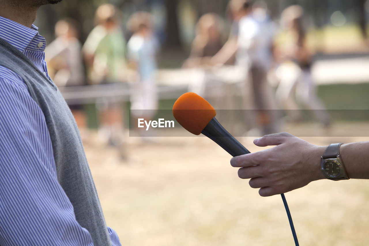 Cropped hand of person holding microphone on the front of man