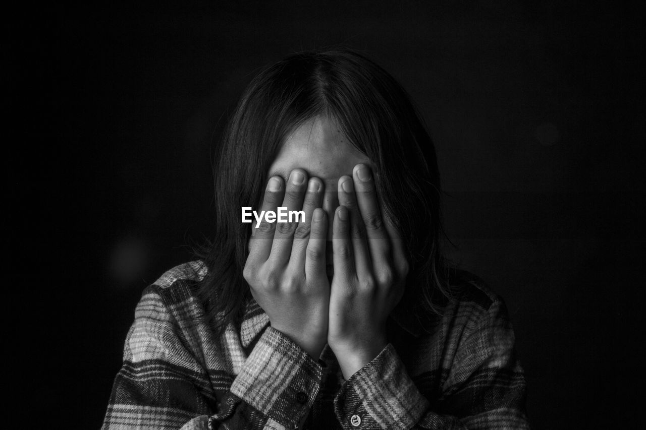 Close-up of person covering face over black background