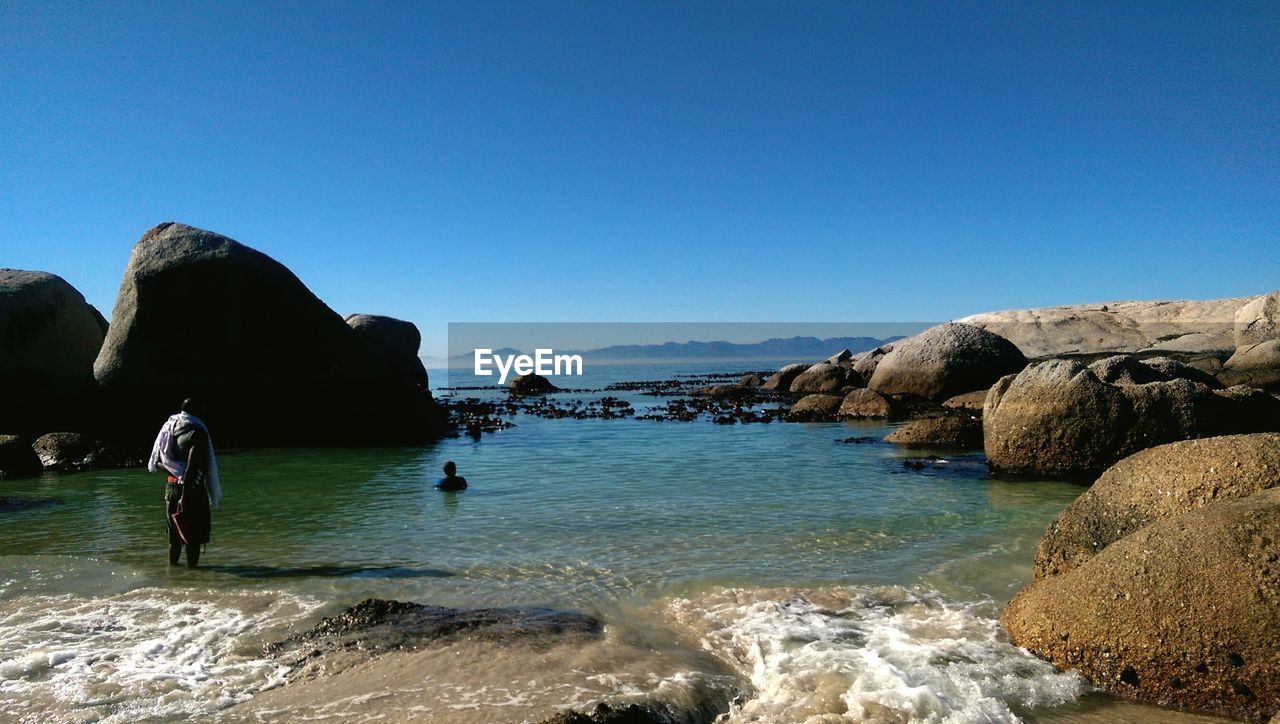 Man standing in sea against clear blue sky during sunny day