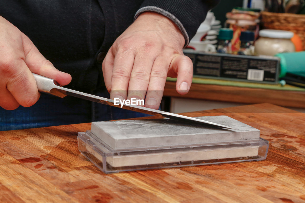 Cropped hand of person sharpening knife on table