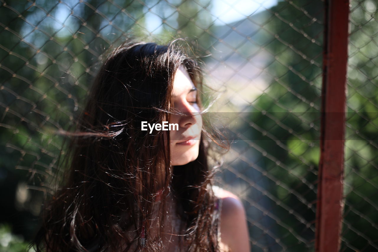 Beautiful woman with eyes closed against chainlink fence