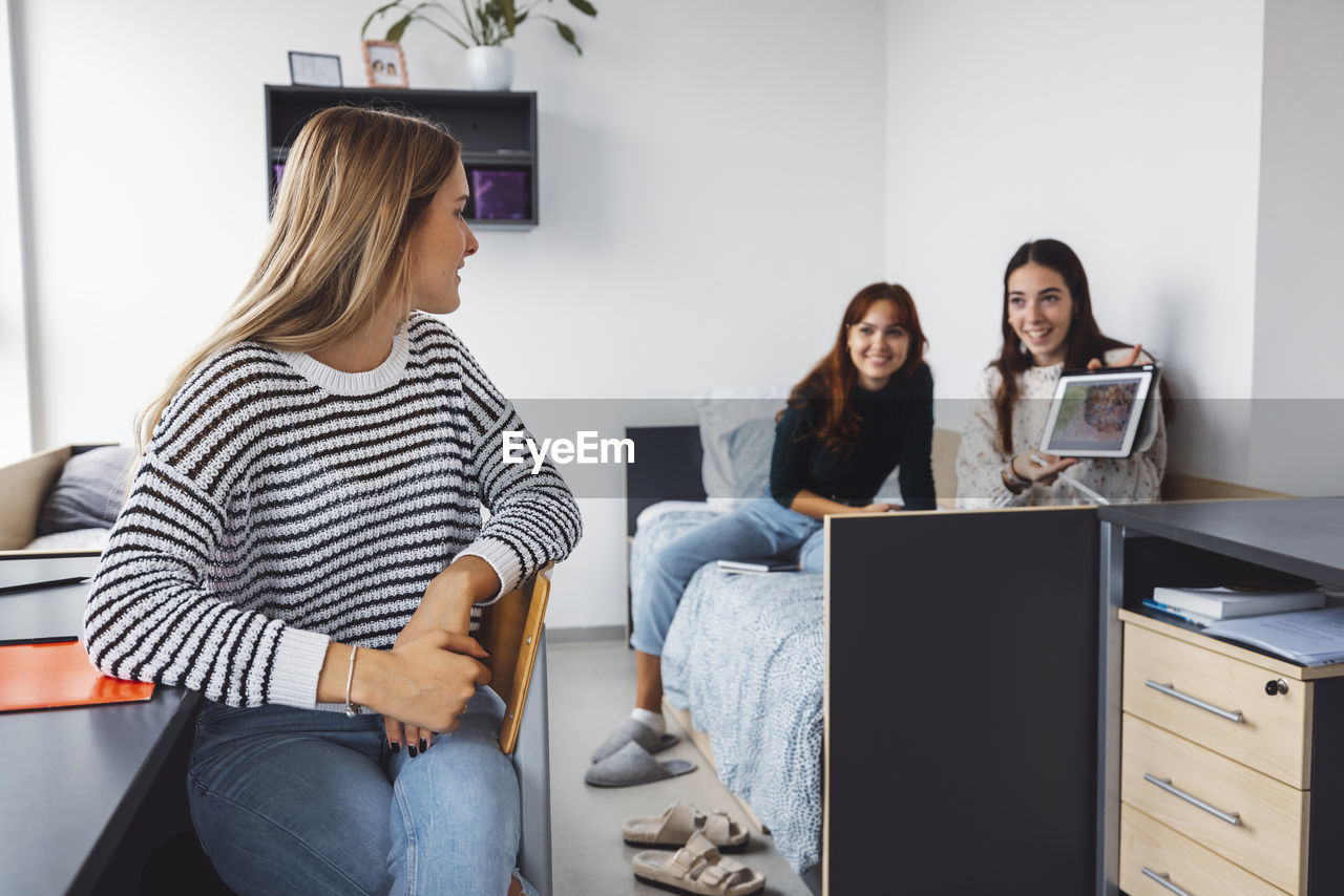 portrait of smiling friends using laptop while sitting at office