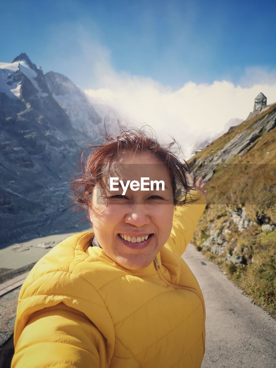 Portrait of smiling mature woman standing on road against blue sky