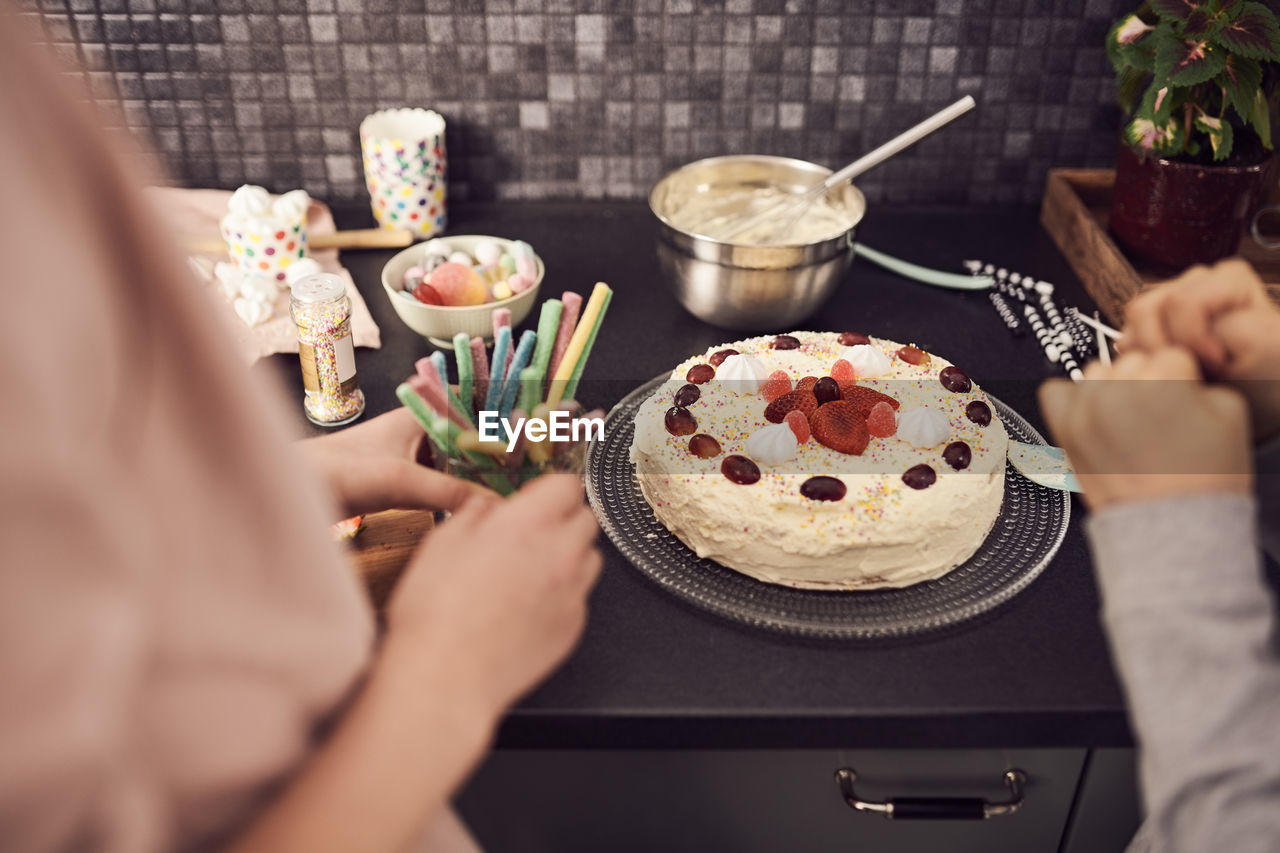 Cropped image of siblings standing by decorated cake at kitchen counter