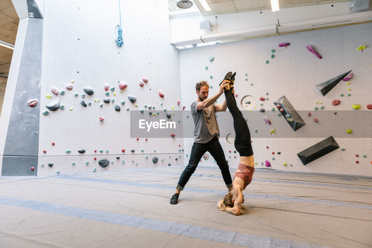 Woman practicing handstand while man holding legs in gym