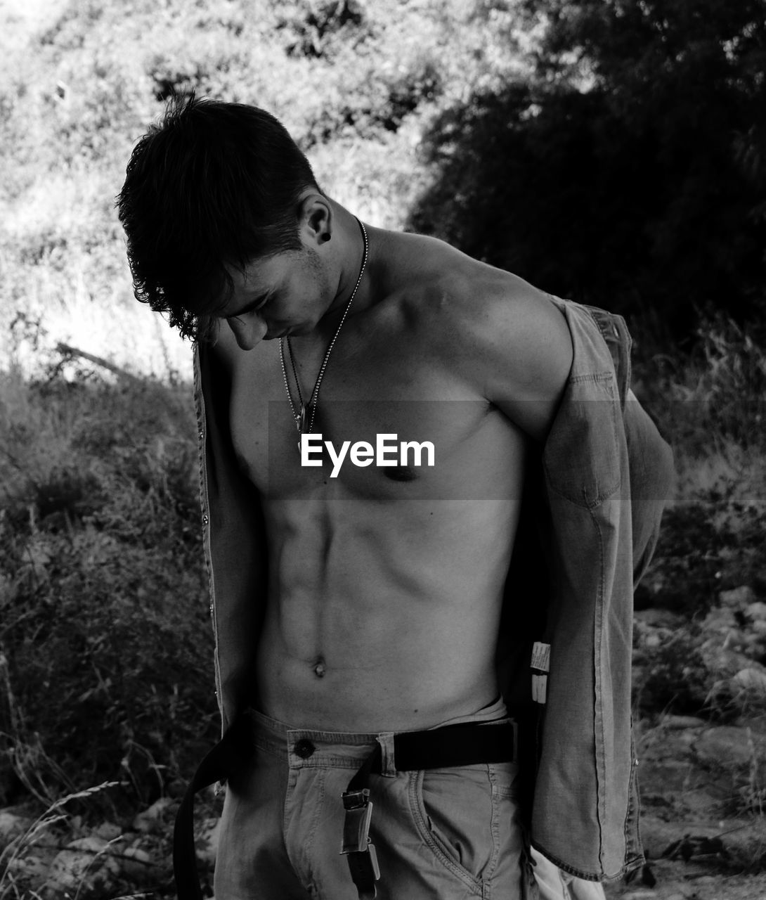 Shirtless young man standing against trees