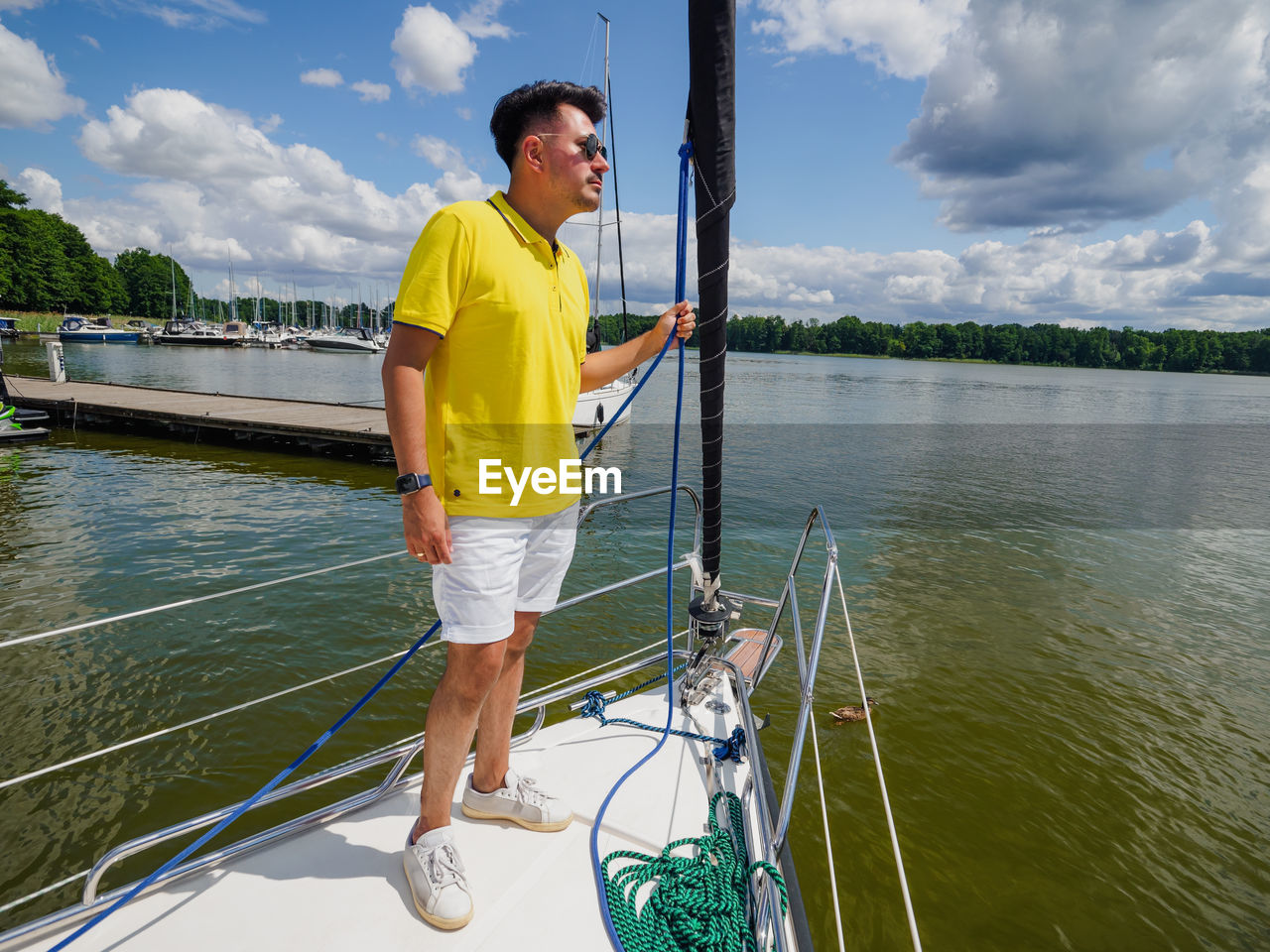 Handsome young person standing on a sailboat bow and looking at side in sunny summer day