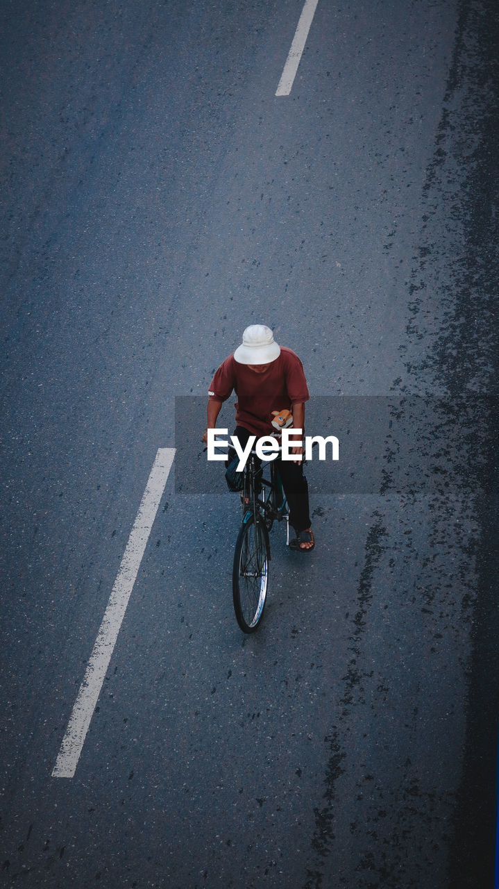 REAR VIEW OF MAN RIDING BICYCLE ON ROAD IN CITY