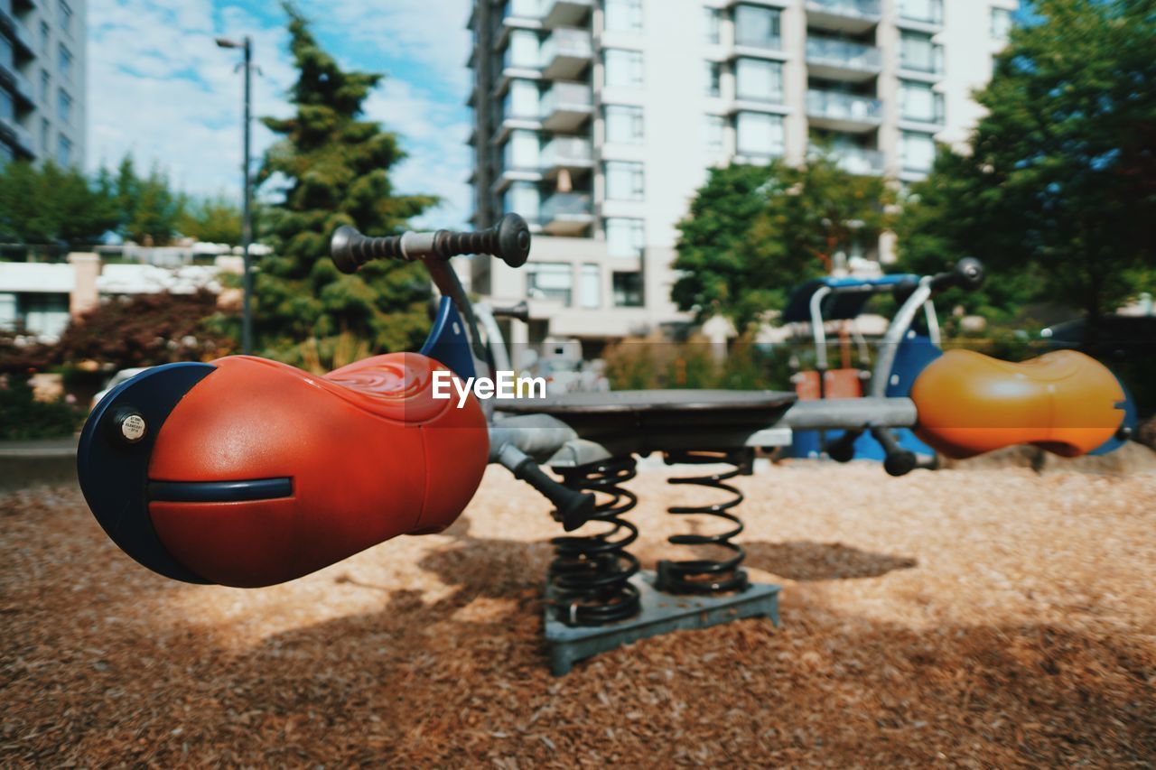 Close-up of spring seesaw in playground against buildings in city